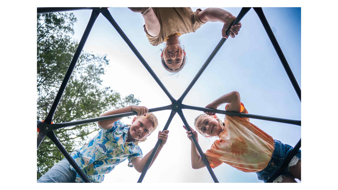 Three kids on top of a climbing dome looking down and smiling.