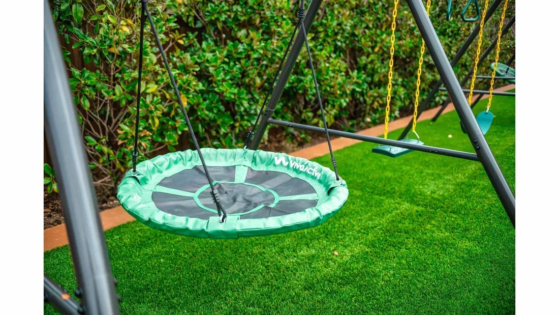 A green and black round saucer swing next to two traditional swings on a large metal swing set.
