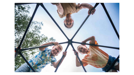Three kids on top of a climbing dome looking down and smiling. 